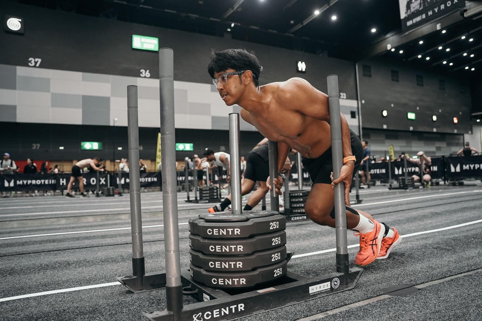 An athlete pushing a weighted sled at an indoor fitness event.